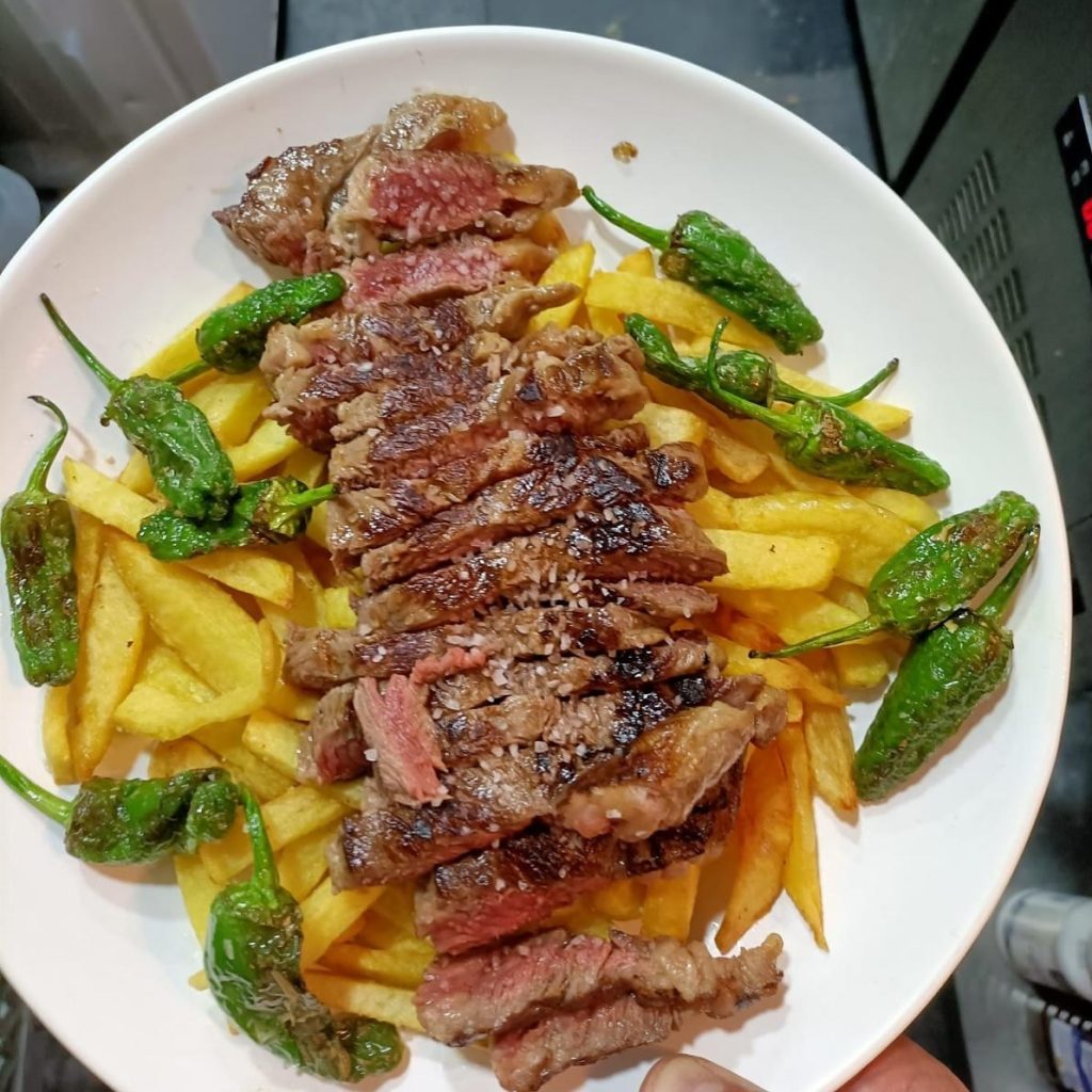 Carne a la plancha cortada en tiras con patatas fritas y pimientos del padrón, tapas originales en Madrid con coins